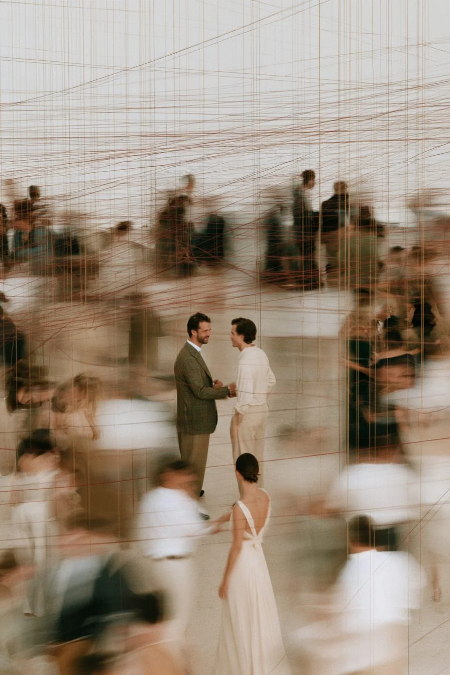 A pale crowd strung with threads, people meeting in pairs