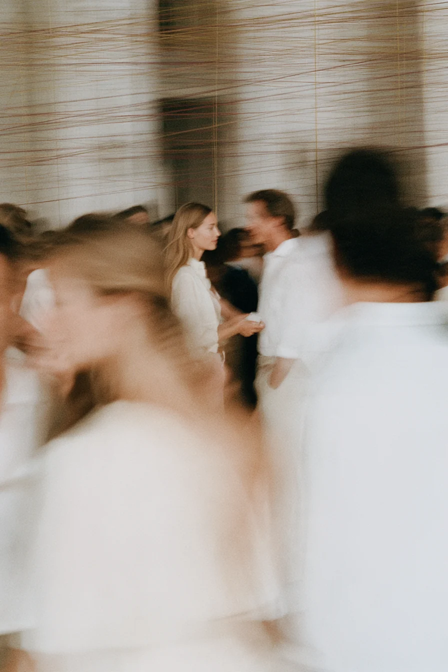 Members in white moving through a pale room strung with fine gold threads, two of them meeting at the centre